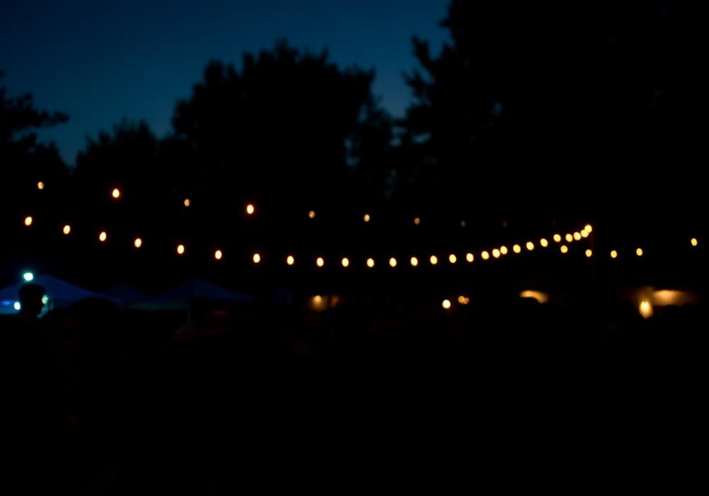 Crowd at a community event lit by warm string lights at dusk